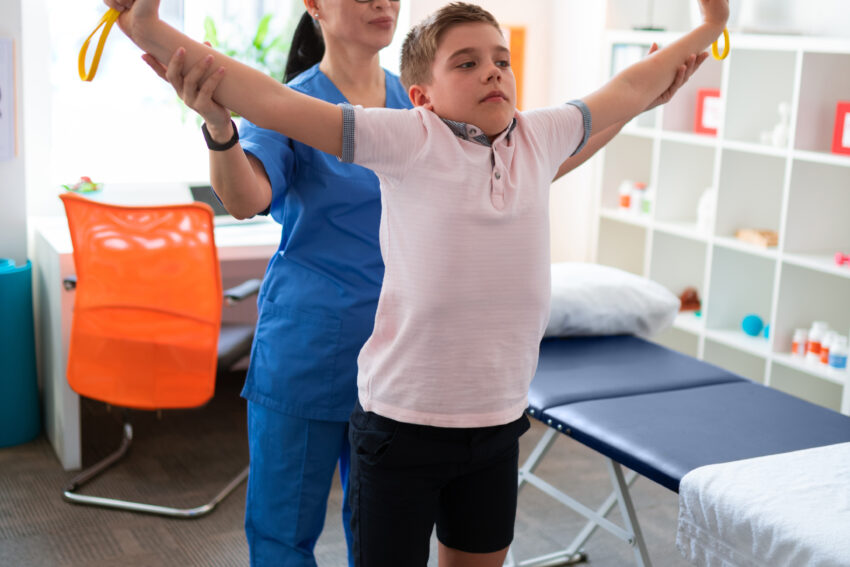 paediatric physiotherapist helping a boy raise his arms and stretch a yellow rope